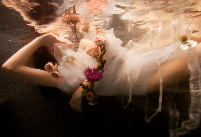 Underwater photograph of a figure in white tulle draped with chrysanthemums and roses